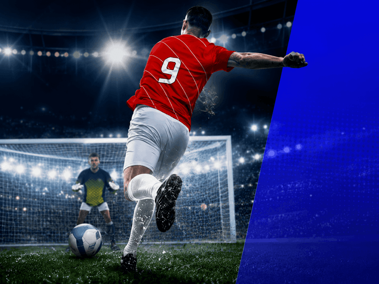 Soccer player wearing a red jersey with the number 9 is about to kick a ball towards the goal, where a goalkeeper in a dark uniform is ready to defend, under bright stadium lights at night.