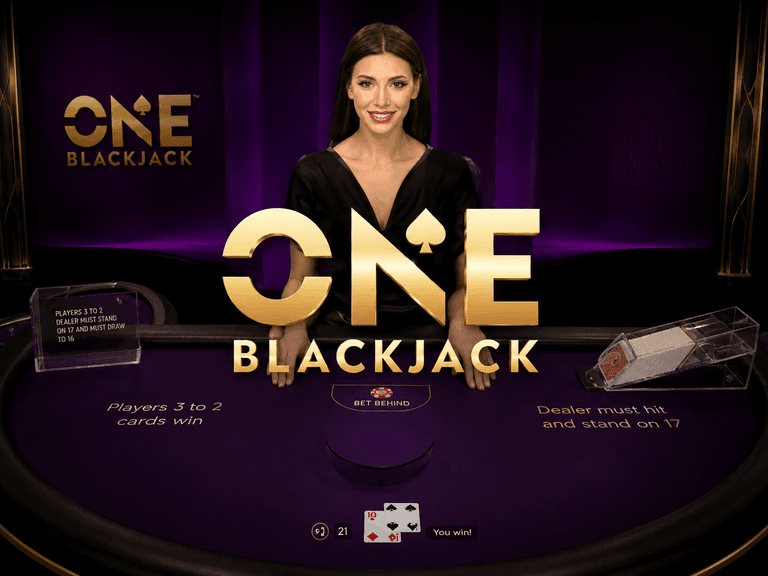 A female dealer stands behind a purple blackjack table with the text "ONE BLACKJACK" prominently displayed in gold letters. Cards showing a blackjack hand and game rules are visible on the table.